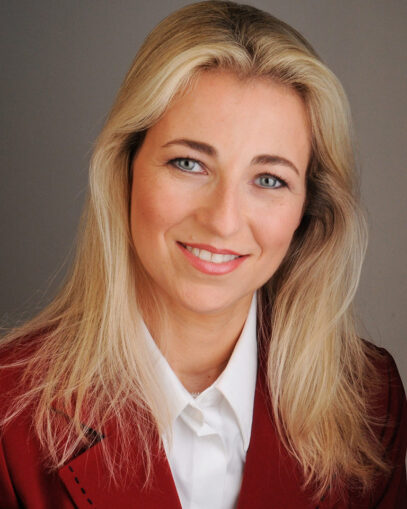 A photograph of Vardit Ravitsky smiling. She is wearing a red blazer and a white collared shirt.