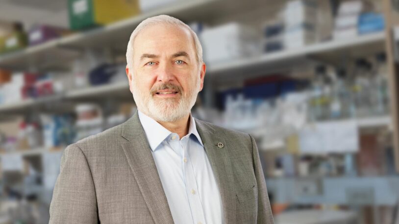 Adrian Krainer in front of shelves filled with laboratory equipment and supplies.