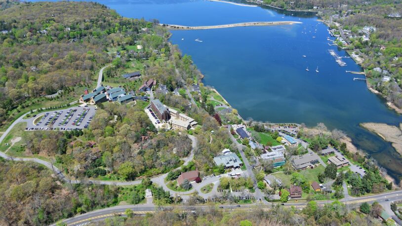Aerial view of a lakeside campus with buildings, parking lots, trees, and boats on the water.