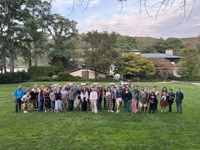 The 2025 CSHL Postdocs poses on a grassy lawn with trees and buildings in the background.
