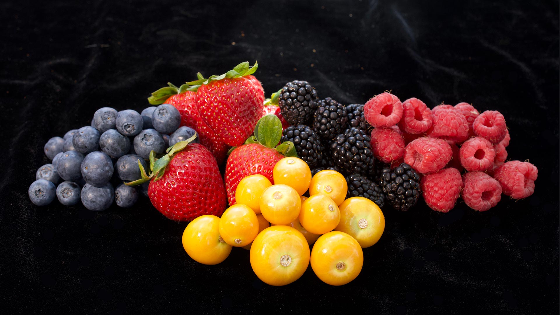 Assorted berries and golden berries arranged on a black surface.
